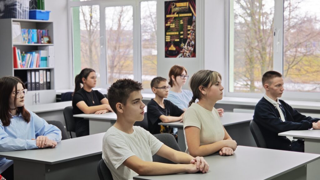 В классе сидят дети за партами, смотрят вперёд. Большие окна, через которые виден зимний пейзаж. На стенах полки с книгами и плакат. В классе сидят дети за партами, смотрят вперёд. Большие окна, через которые виден зимний пейзаж. На стенах полки с книгами и плакат.