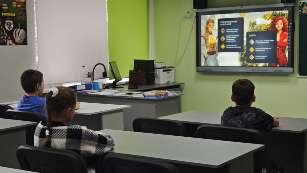 В классе трое детей сидят за партами и смотрят на экран проектора. На стенах зелёные обои, на партах лежат книги и тетради. В классе трое детей сидят за партами и смотрят на экран проектора. На стенах зелёные обои, на партах лежат книги и тетради.