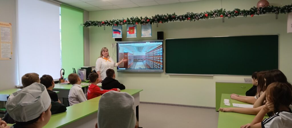 В классе дети сидят за партами, слушают учителя. На стене экран, на нём видео. Класс украшен гирляндой. В классе дети сидят за партами, слушают учителя. На стене экран, на нём видео. Класс украшен гирляндой.